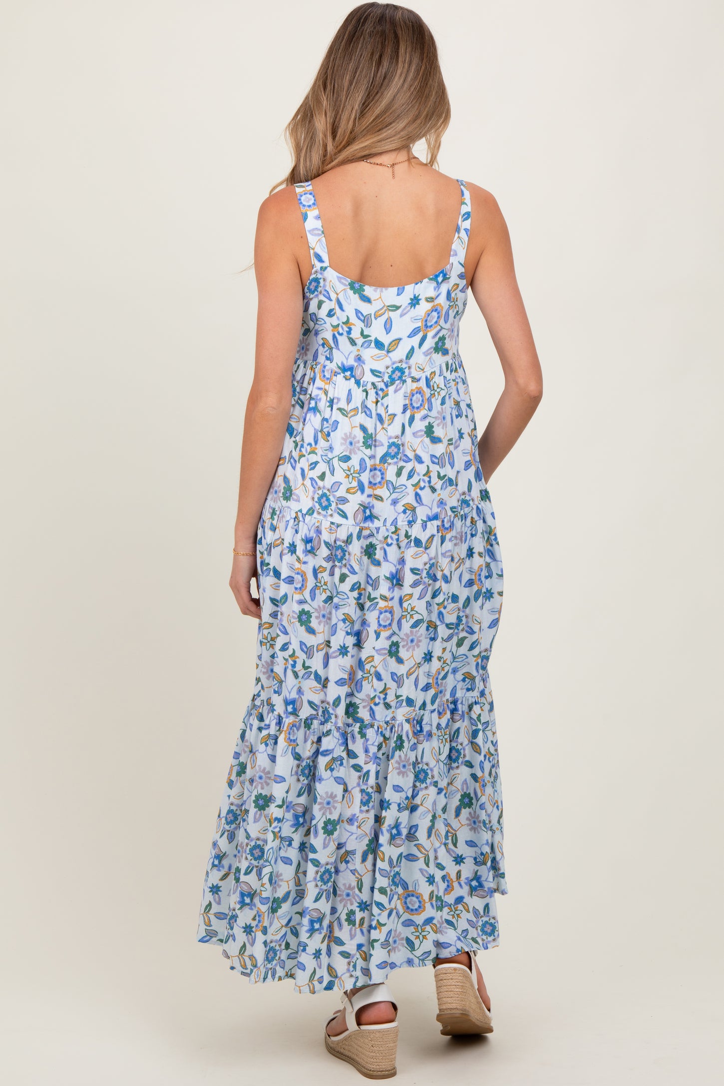 woman wearing a floral blue maternity maxi dress with a tiered ruffle hem, showing her back and straps