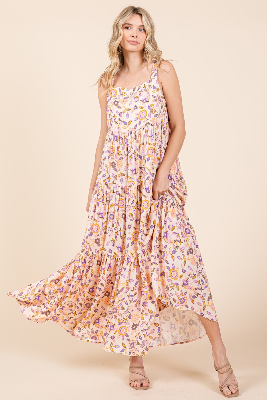 woman wearing a floral maxi dress with a tiered design and spaghetti straps, standing against a neutral background