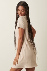 woman wearing a beige short sleeve ribbed dress, showing a relaxed fit and a playful pose from behind