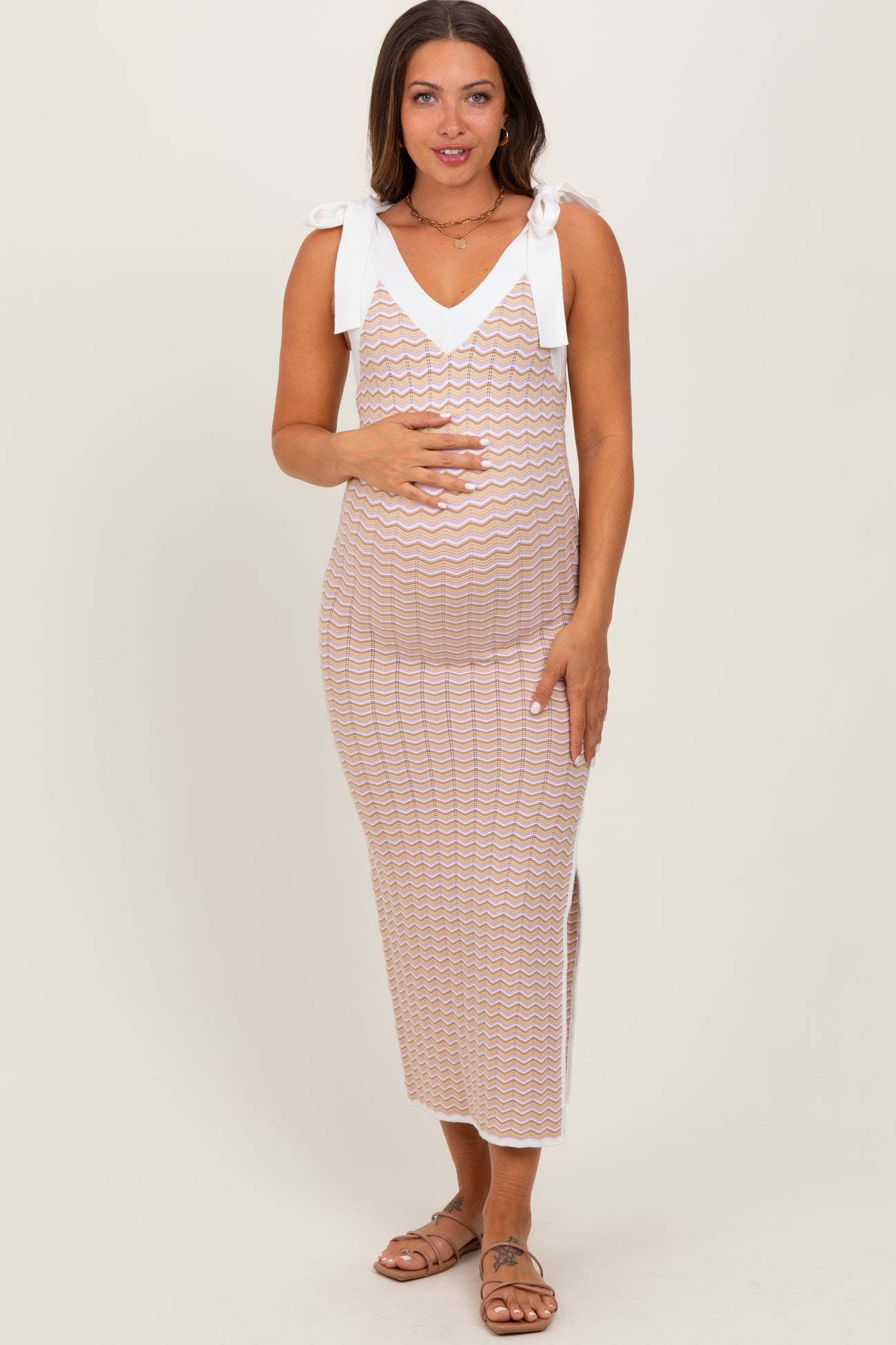 woman wearing a cream and multi-colored zigzag patterned maternity dress with tie straps and a visible baby bump