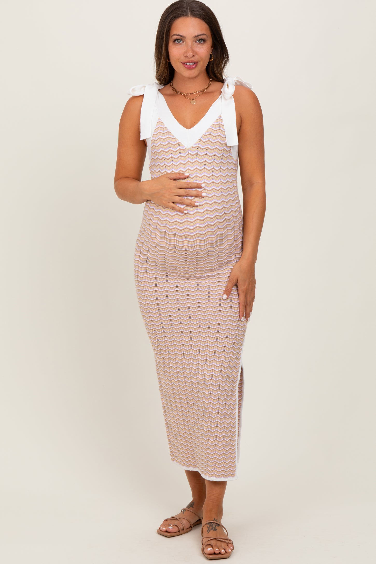 woman wearing a cream and multi-colored zigzag patterned maternity dress with tie straps and a visible baby bump
