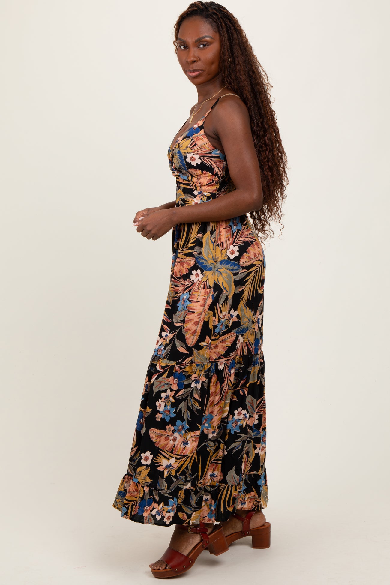 woman wearing a black floral maxi dress with adjustable straps and tiered hem, posing sideways