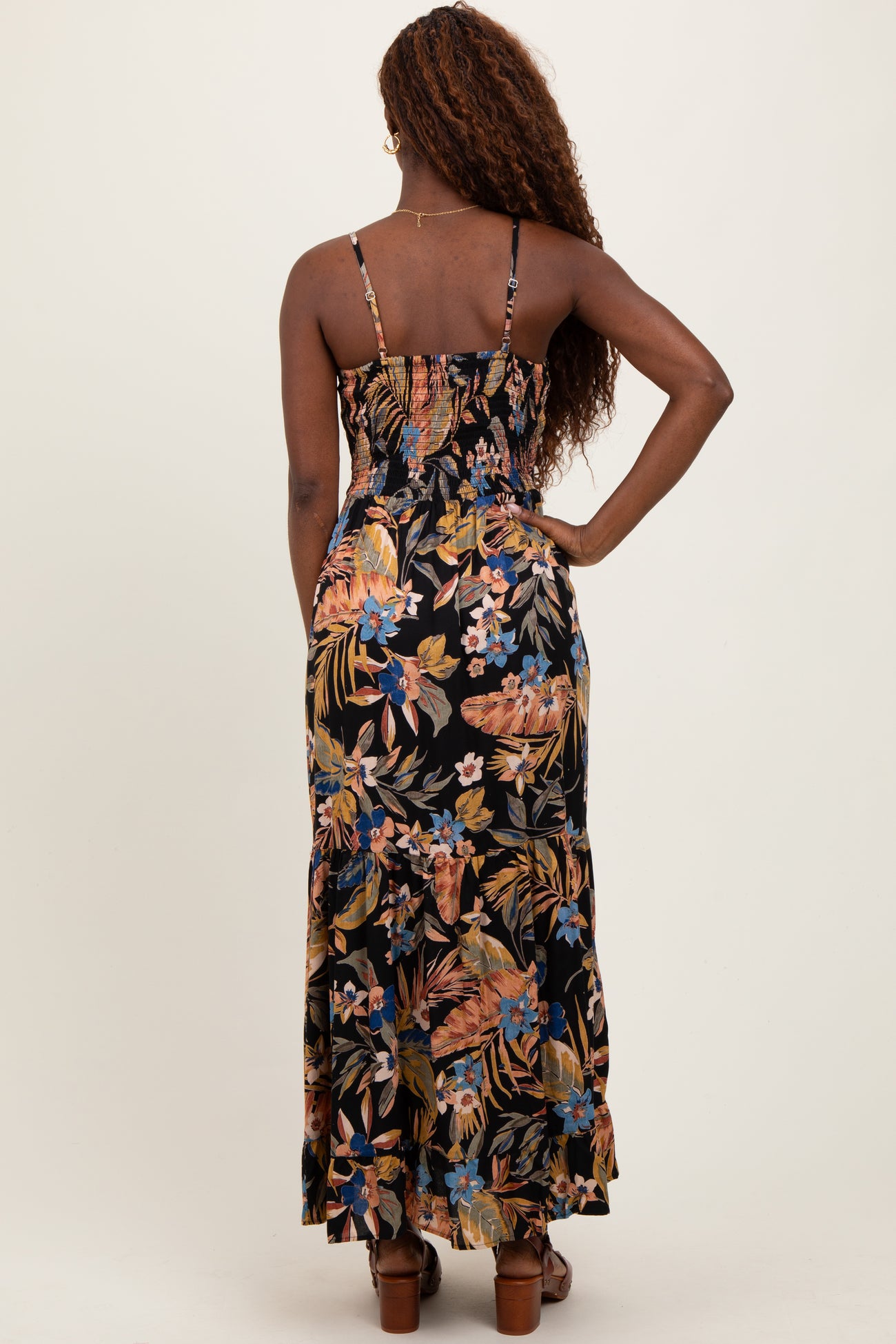 woman wearing a black floral maxi dress with adjustable straps and a smocked back detail, standing with her back to the camera