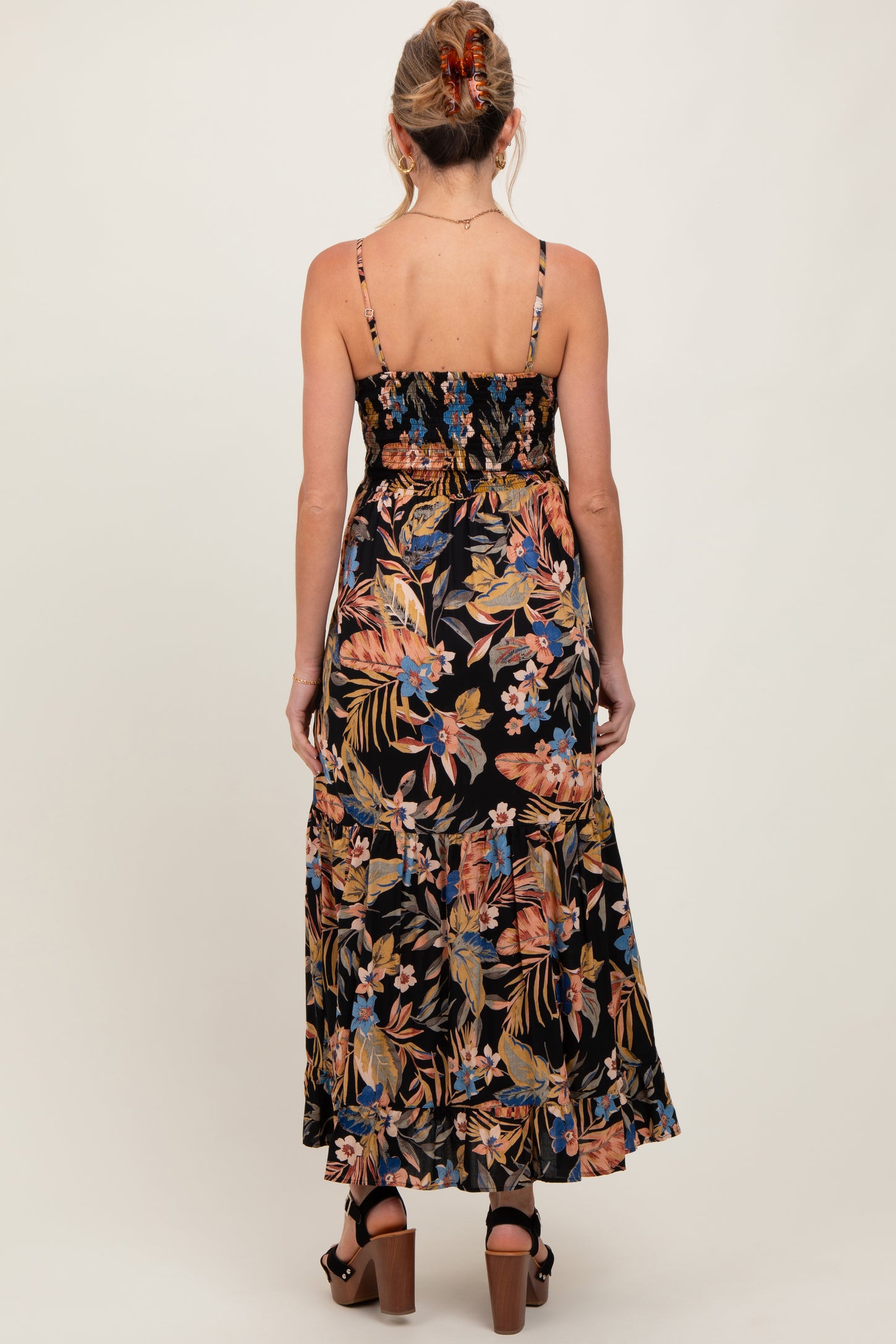 woman wearing a black floral maternity maxi dress with adjustable straps and a tiered skirt from the back