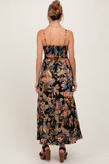 woman wearing a black floral maternity maxi dress with adjustable straps and a tiered skirt from the back
