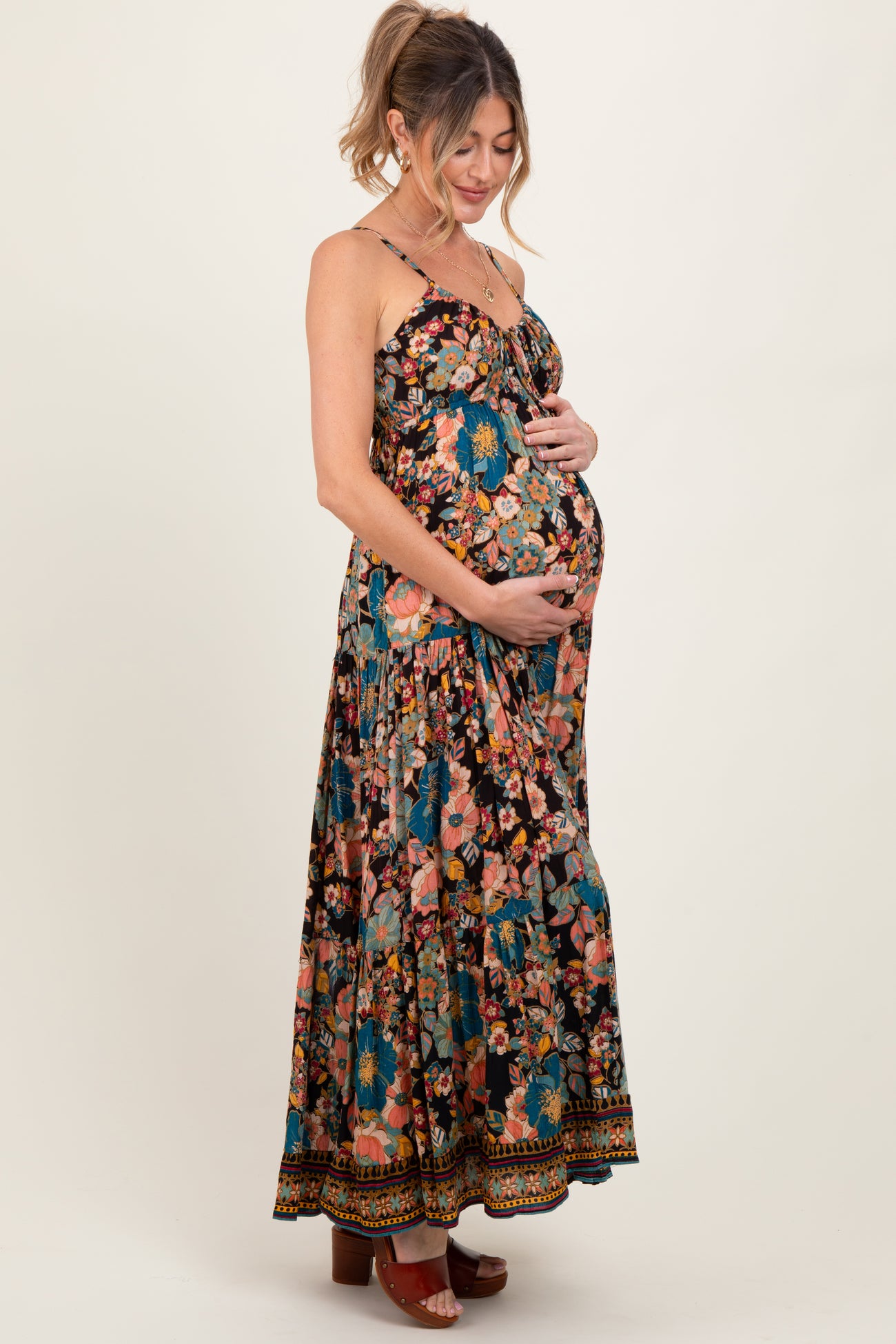 woman wearing a black floral maternity maxi dress with a sweetheart neckline and holding her baby bump