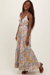woman wearing a floral maxi dress with a deep v-neckline and a tiered skirt, smiling and standing against a plain background