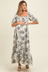 woman wearing a black and white floral print maternity maxi dress and holding her baby bump