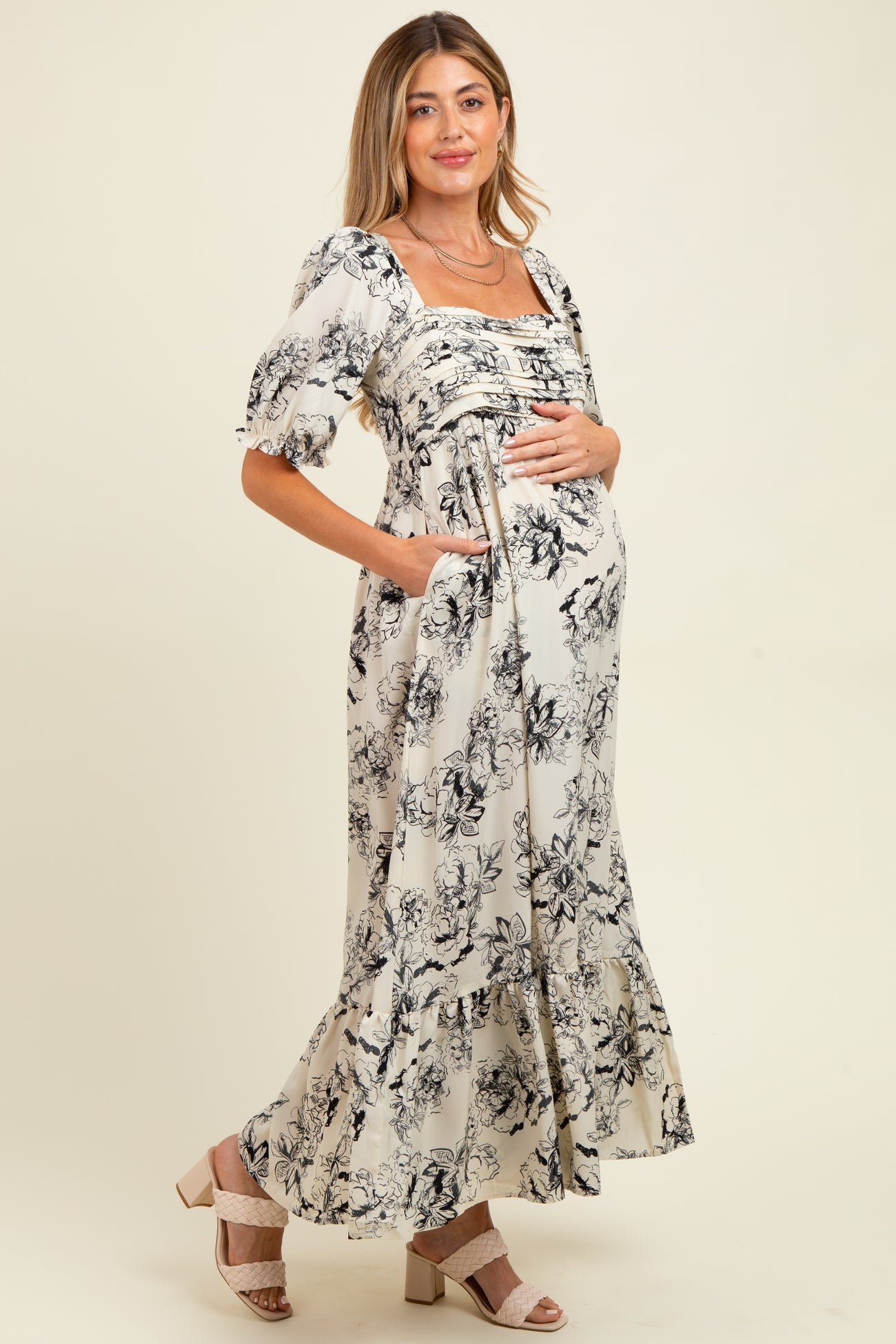 woman wearing a floral print maternity maxi dress with puff sleeves and a baby bump, posing with hands on her belly