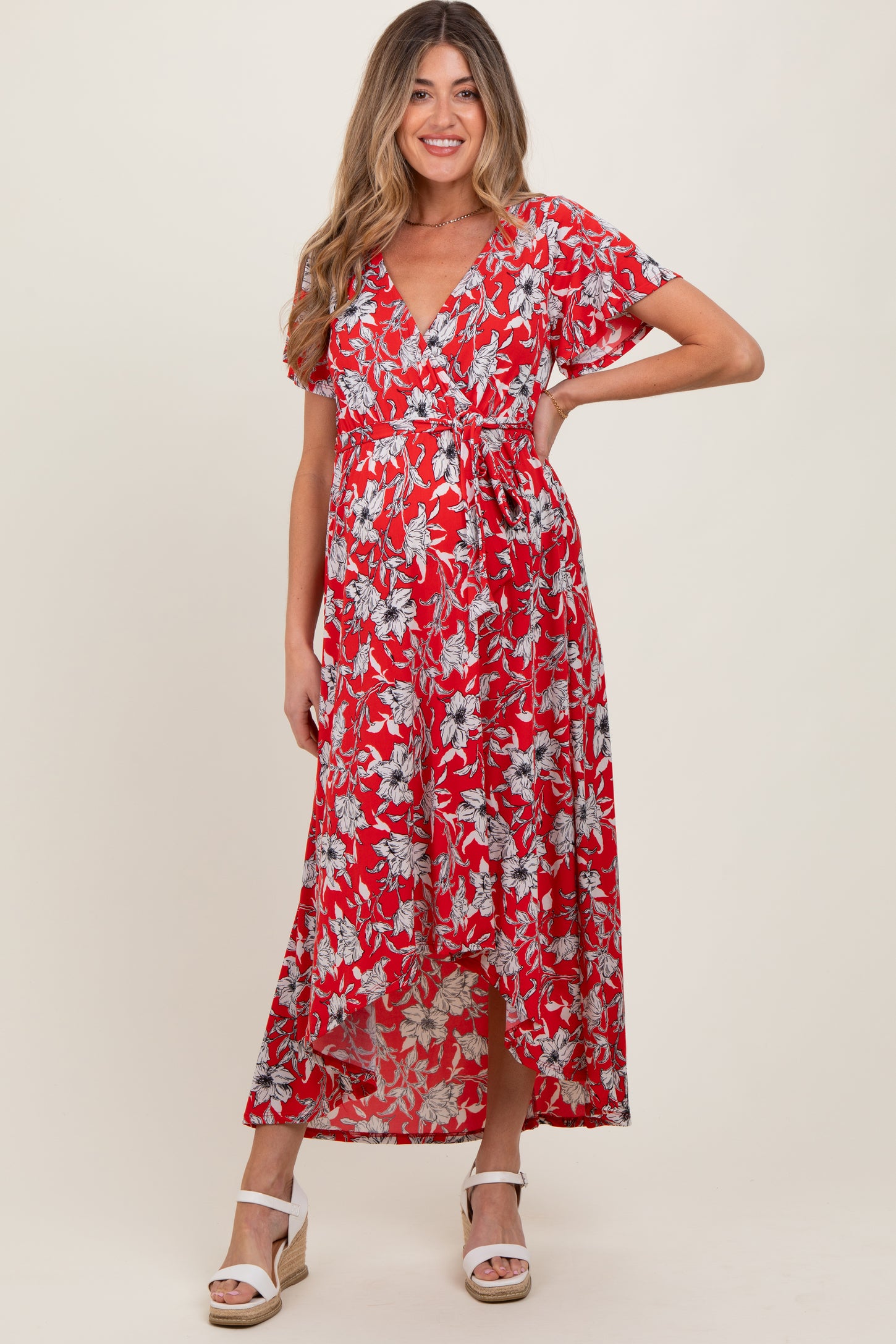 woman wearing a red floral print maternity maxi dress with short sleeves and a tie waist, showing her baby bump
