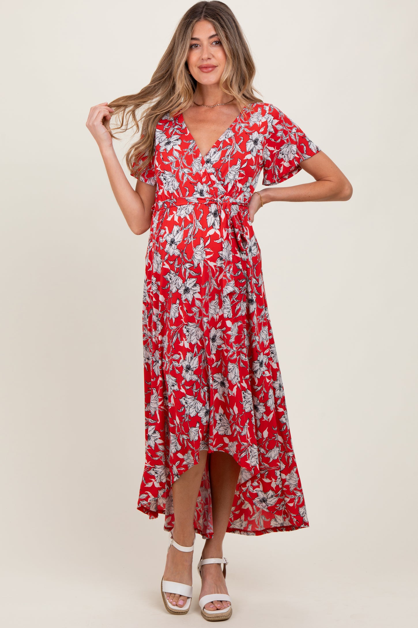 woman wearing a red floral maternity dress with a wrap style and high-low hem, showcasing her baby bump
