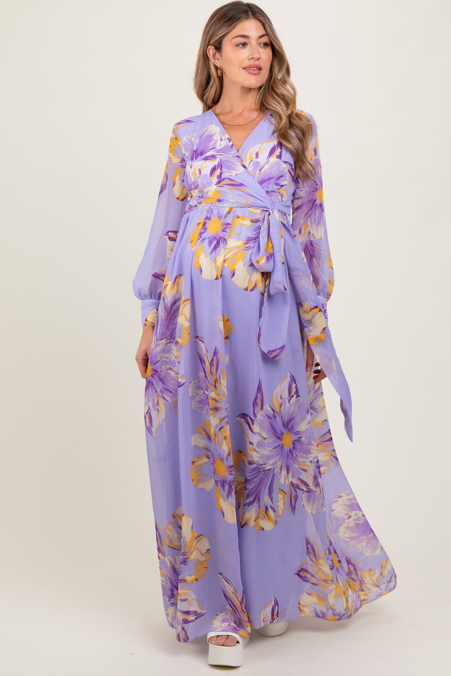woman wearing a lavender floral maternity maxi dress with a wrap style and long sleeves, showcasing her baby bump