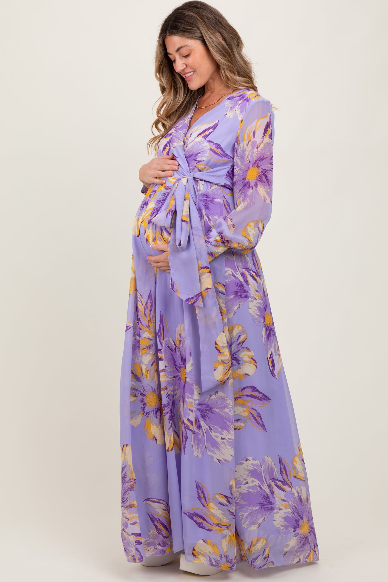 woman wearing a purple floral maternity maxi dress and gently holding her baby bump