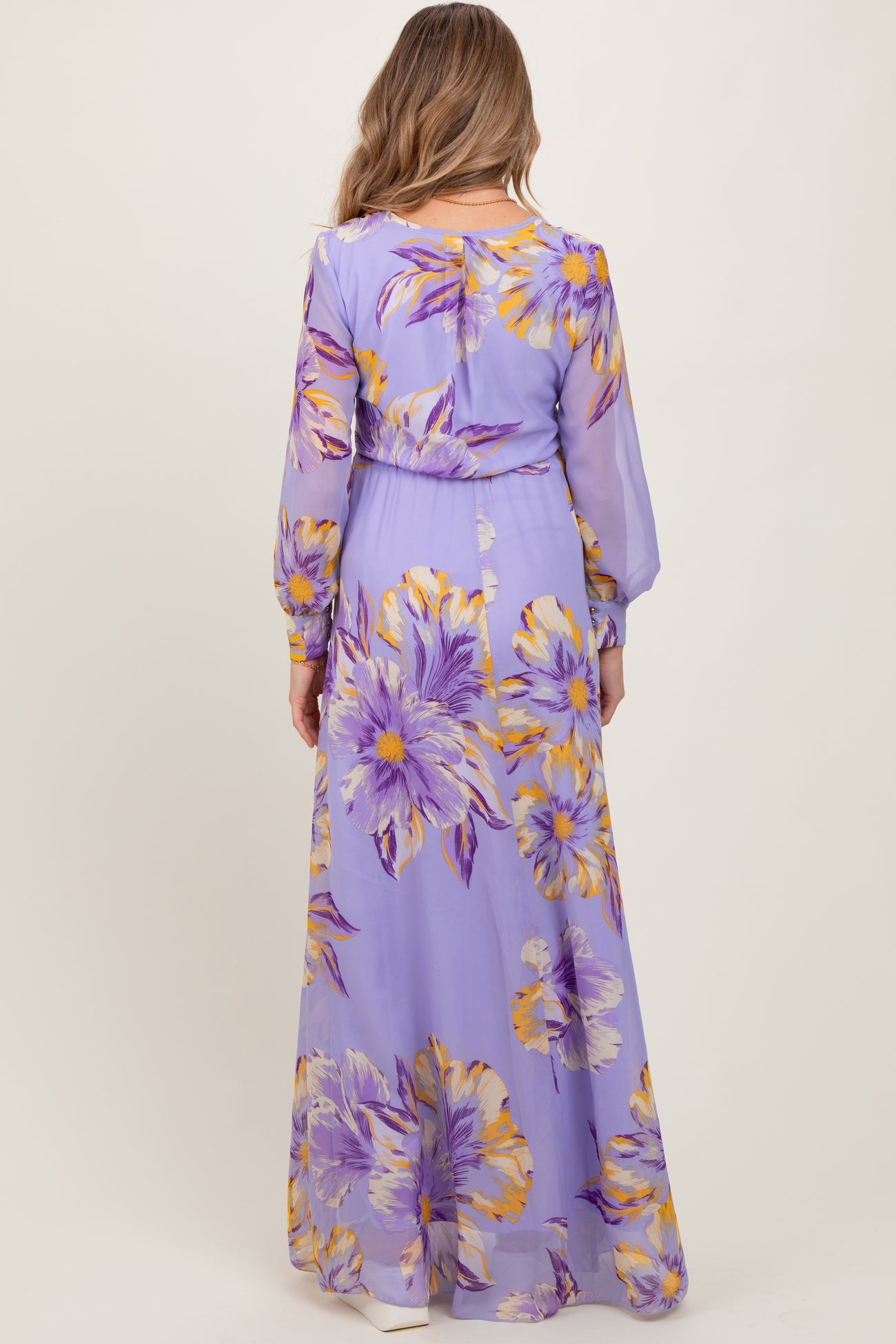 woman wearing a purple floral print maternity dress with long sleeves and a flowing skirt