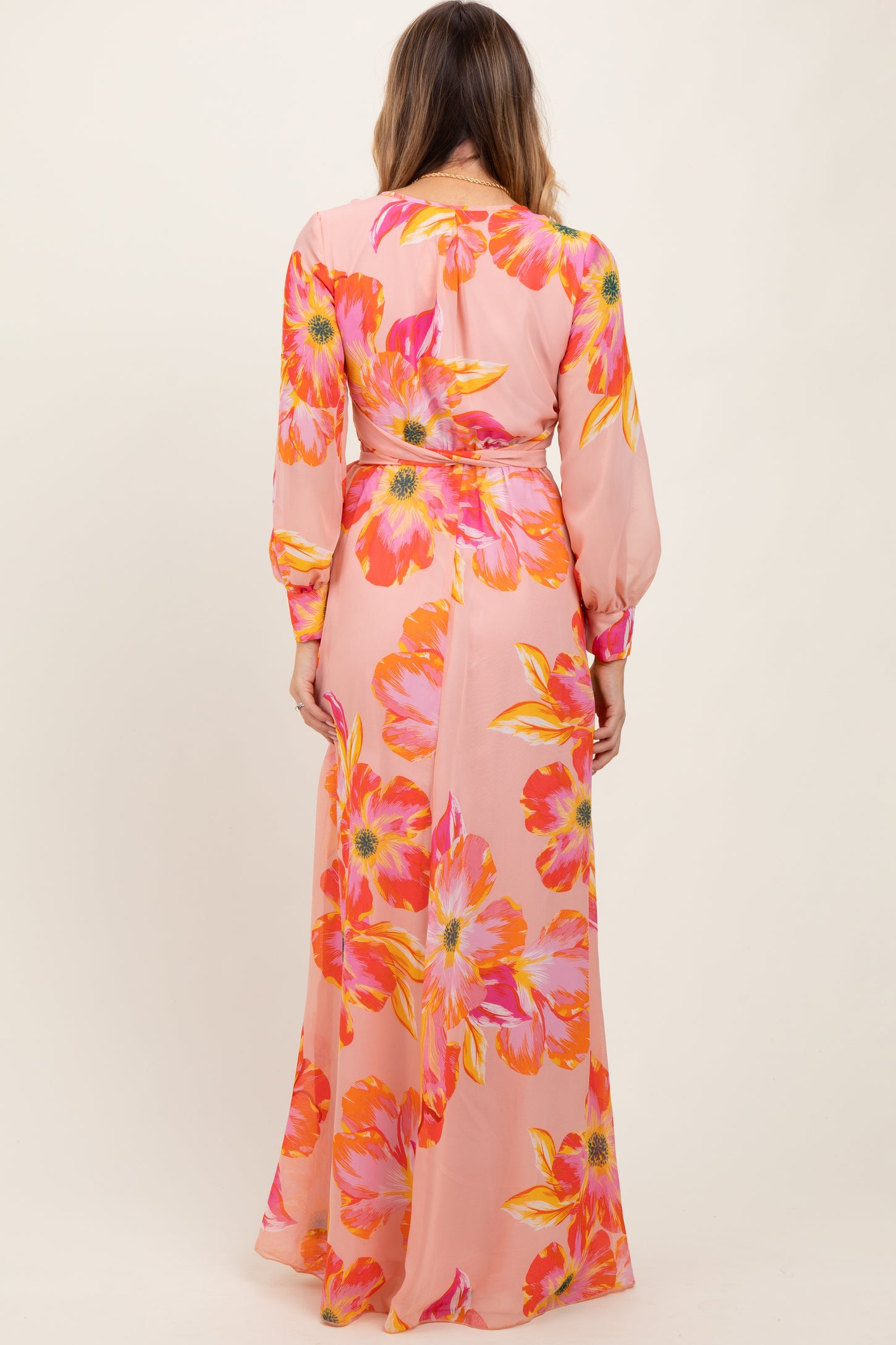 woman wearing a pink floral maxi dress with long sleeves and a cinched waist seen from the back