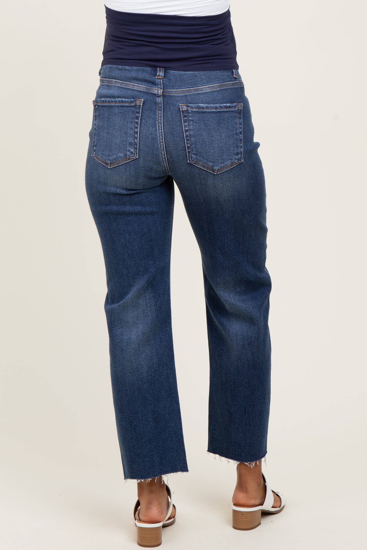 woman wearing dark wash maternity jeans with a frayed hem and a fitted waist, showing a visible baby bump