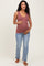 woman wearing a rust colored maternity tank top and distressed blue jeans, holding her baby bump