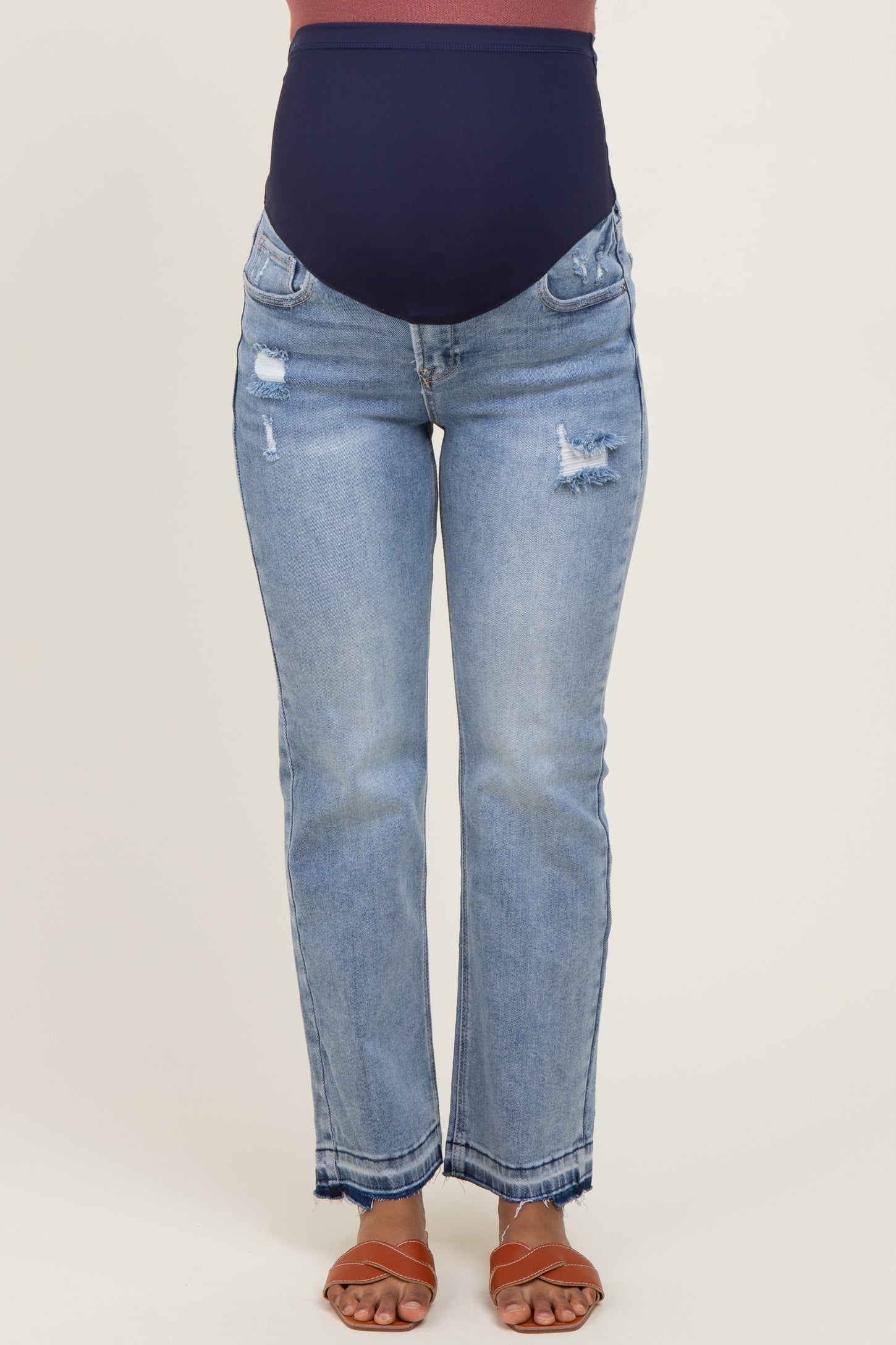 woman wearing distressed light blue maternity jeans with a dark blue over-the-belly waistband and brown sandals