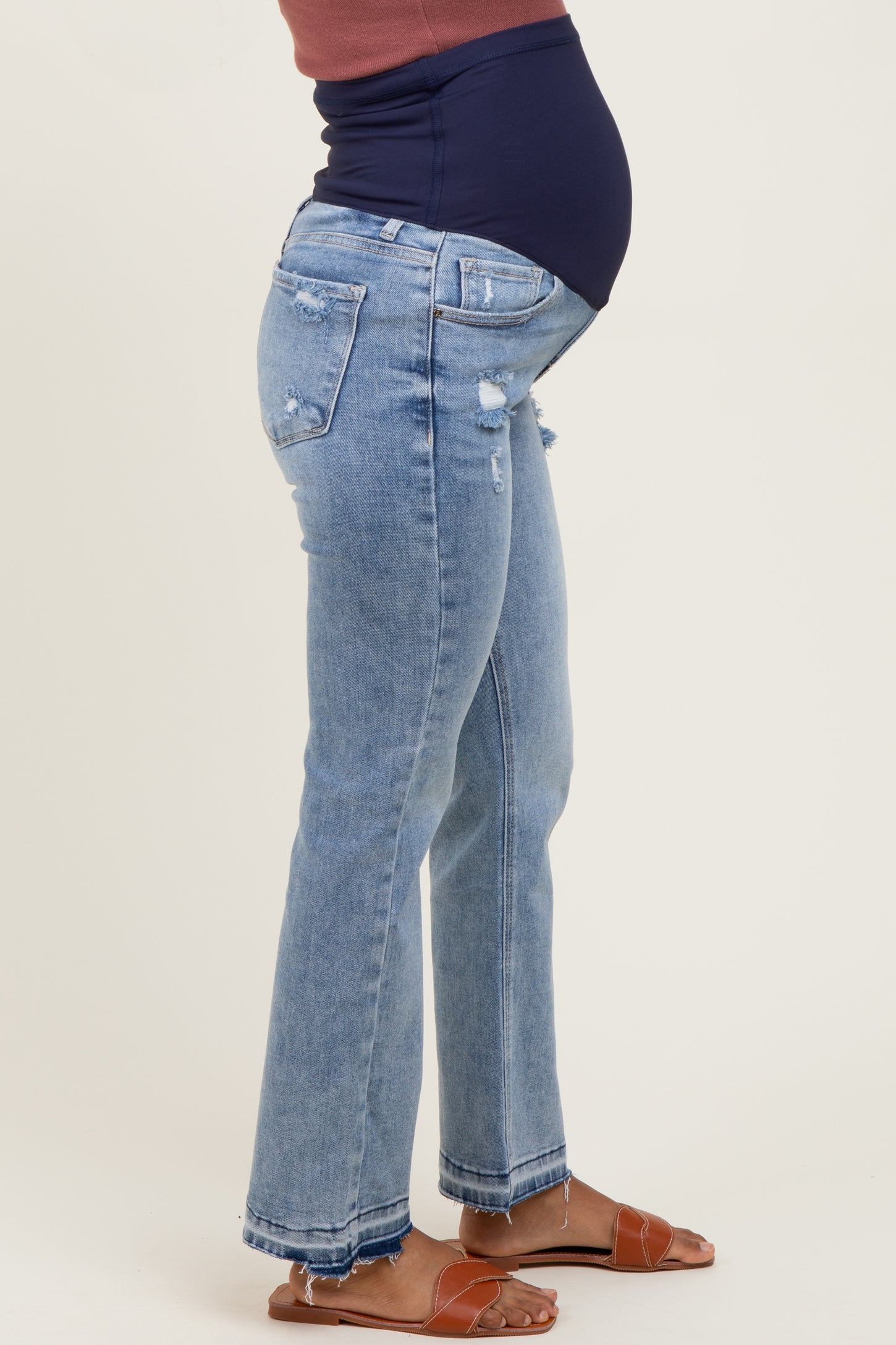 woman wearing distressed light blue maternity jeans with a navy blue over-the-bump panel and a baby bump visible