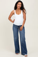 woman wearing a white maternity tank top and blue flared maternity jeans, showing her baby bump