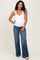 woman wearing a white maternity tank top and blue flared maternity jeans, showing her baby bump