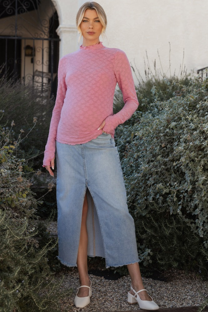 woman wearing a pink long sleeve maternity top with thumbholes and a light blue denim maxi skirt, showcasing her baby bump