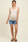 woman wearing a beige maternity tank top and denim shorts, showing her baby bump
