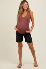 woman wearing a rusty pink maternity tank top and black maternity shorts, showing her baby bump while posing with hands in pockets