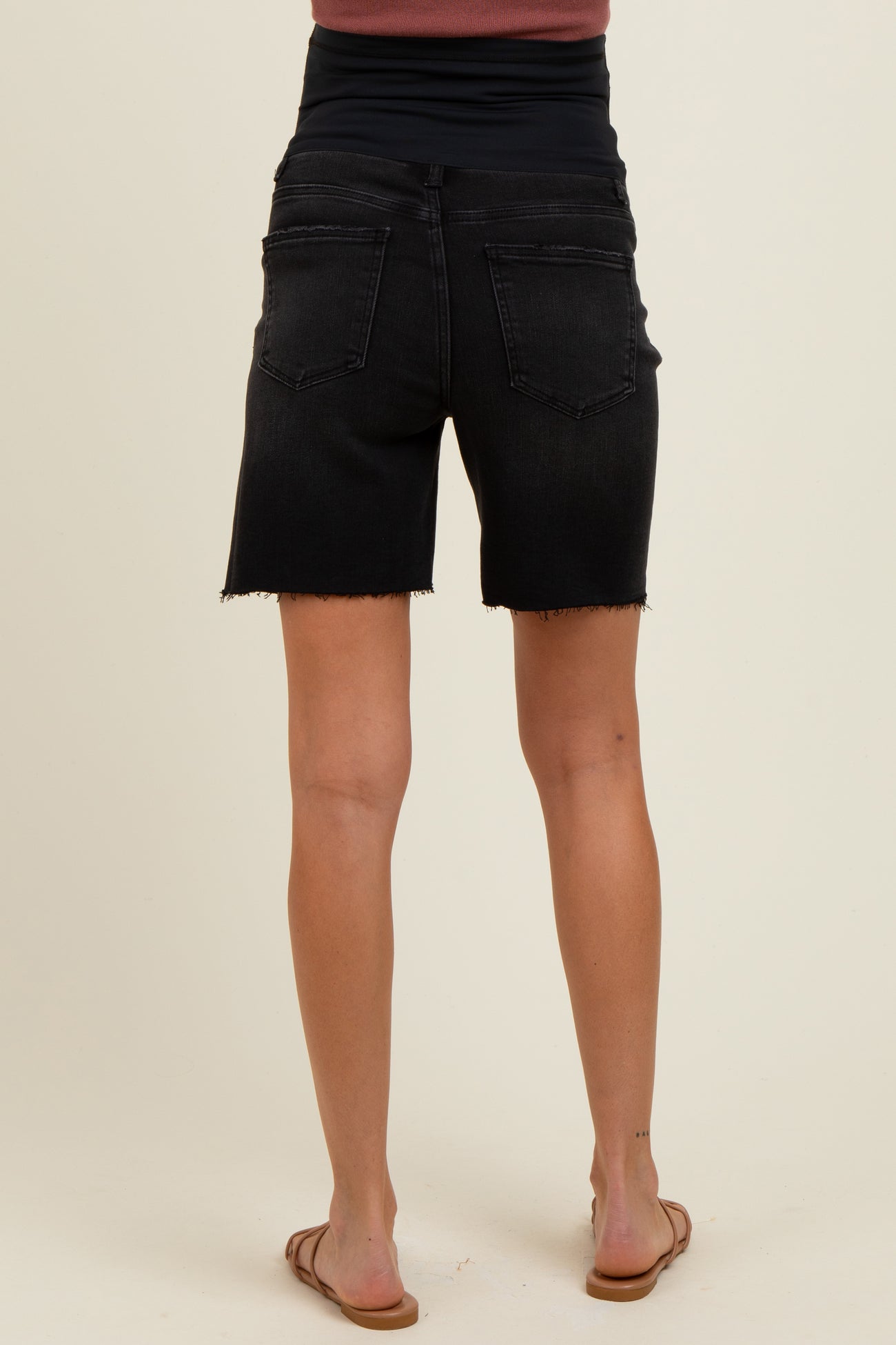 woman wearing black maternity denim shorts with a frayed hem, showing the back view and a comfortable fit