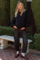 woman wearing a black maternity sweater with puffed sleeves and dark denim maternity jeans, showcasing her baby bump
