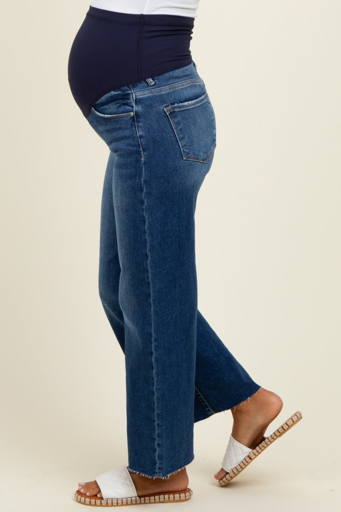 woman wearing dark blue maternity jeans with a high waistband, showing a visible baby bump, paired with white sandals