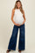 woman wearing a fitted cream maternity tank top and wide-leg dark wash maternity jeans, holding her baby bump