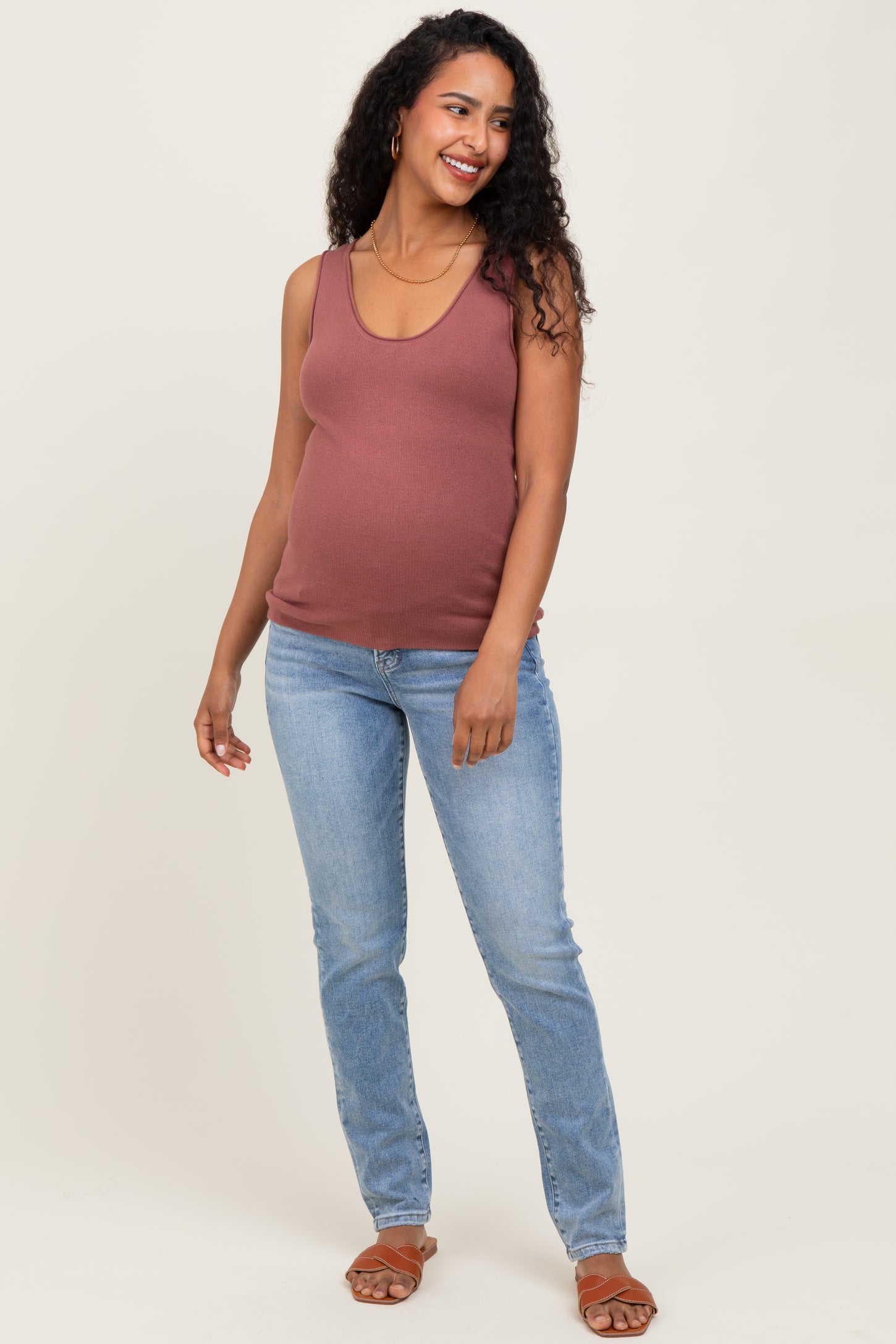woman wearing a dusty rose maternity tank top and blue jeans, smiling with her baby bump visible