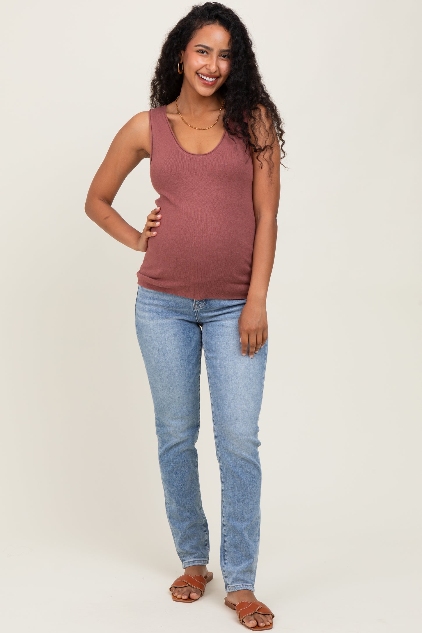 woman wearing a rust-colored maternity tank top and blue skinny jeans, showing her baby bump