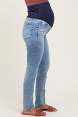 woman wearing light blue maternity jeans with a baby bump visible, paired with a dark blue top and brown sandals