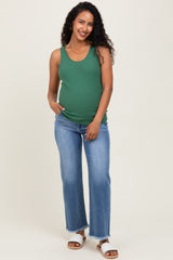 woman wearing a green ribbed maternity tank top and blue flared jeans, showing her baby bump