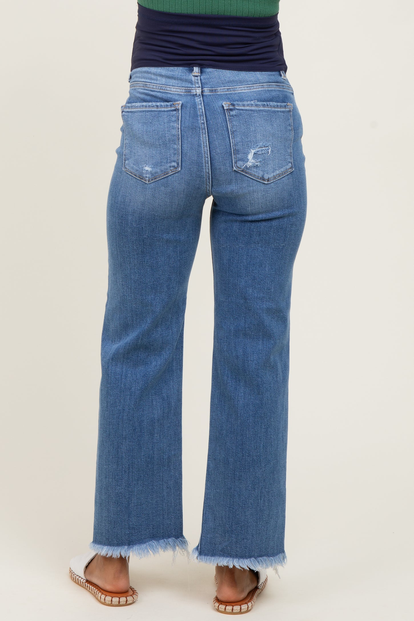 woman wearing light blue maternity flared jeans with frayed hem and distressed details, view from the back