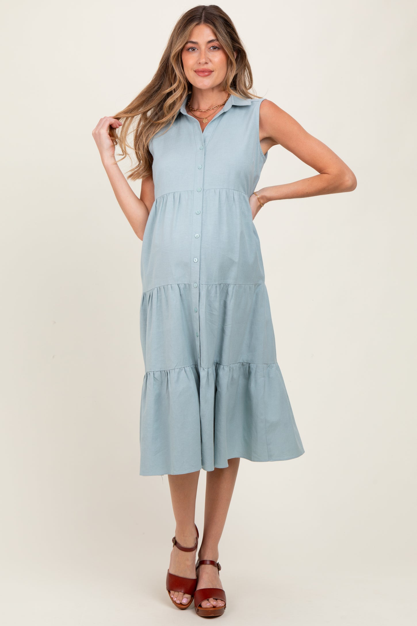 woman wearing a light blue sleeveless maternity dress with a button-down front and tiered skirt, showcasing her baby bump