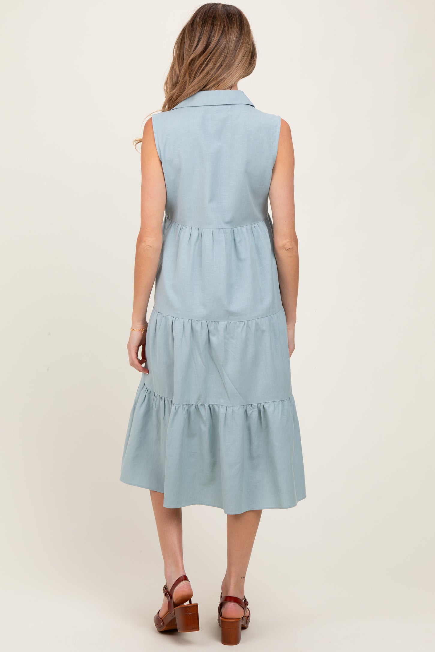 woman wearing a light blue sleeveless maternity dress with a tiered skirt and a collared neckline from the back