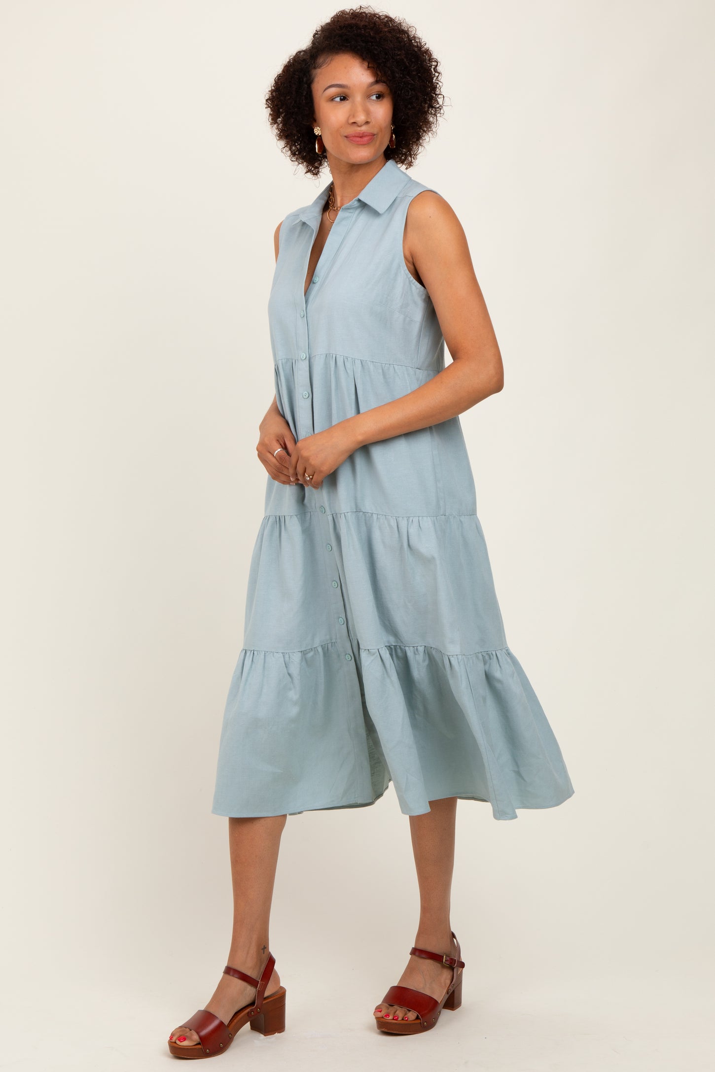woman wearing a light blue sleeveless button-down midi dress with a tiered skirt and brown heeled sandals