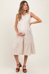 woman wearing a beige sleeveless maternity dress with buttons and tiered ruffles, holding her baby bump