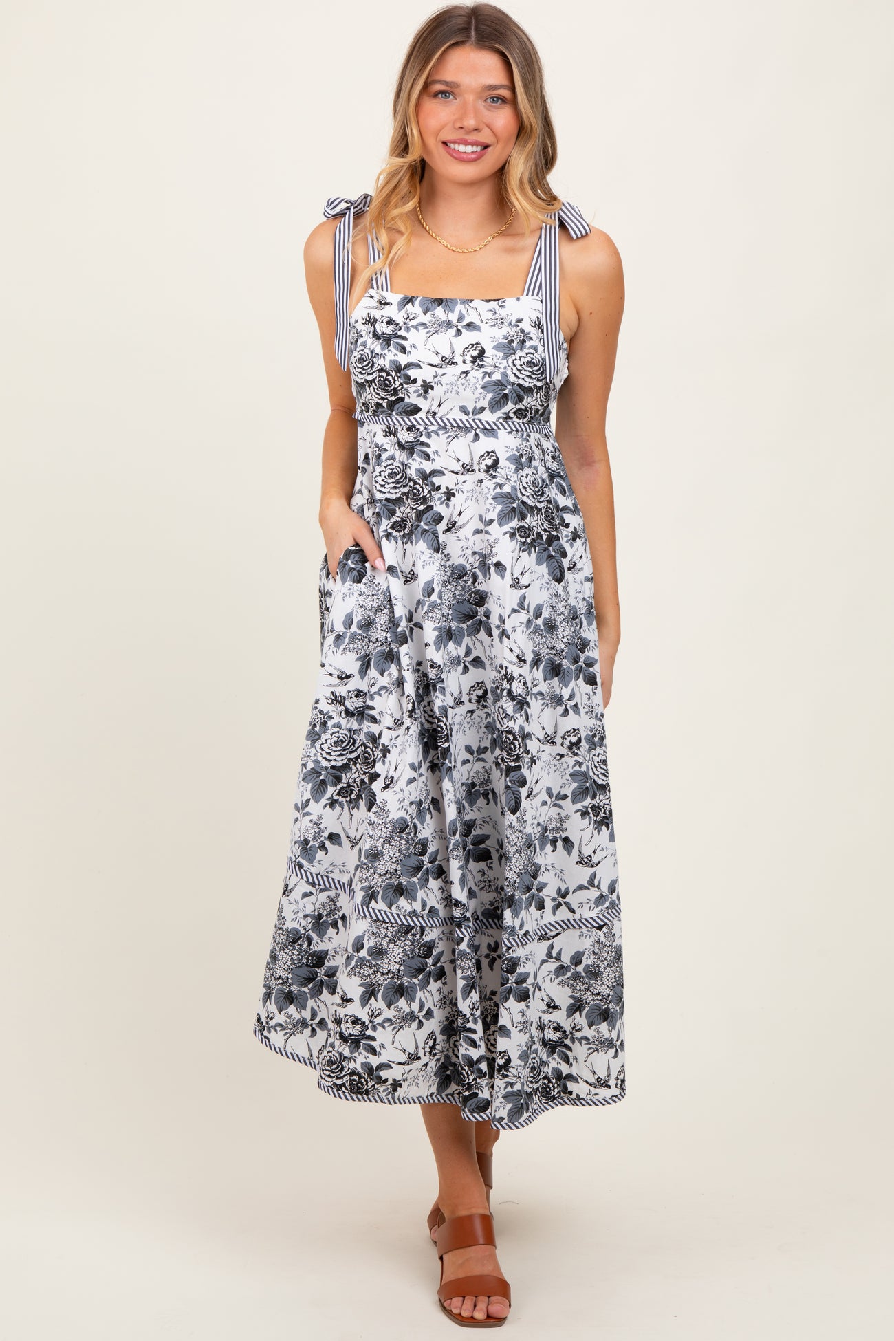 woman wearing a floral print maxi dress with blue and white stripes and bow shoulder straps, pockets visible