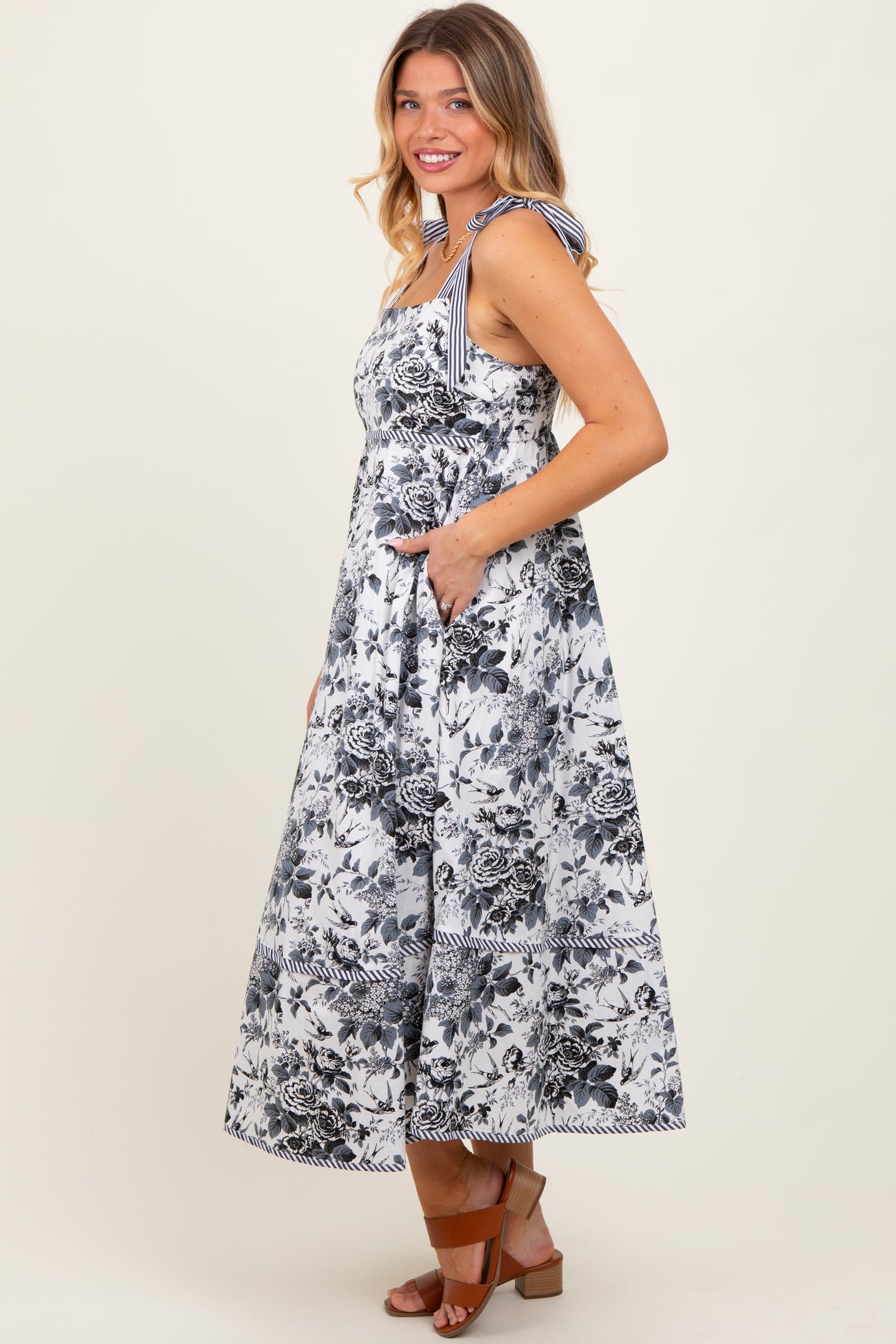 woman wearing a floral print maxi dress with tie shoulder straps and pockets, standing sideways