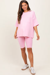 woman wearing a pink oversized t-shirt and matching bike shorts, showcasing a casual maternity outfit