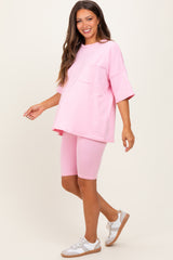 woman wearing a light pink maternity oversized t-shirt and matching biker shorts, posing with a smile