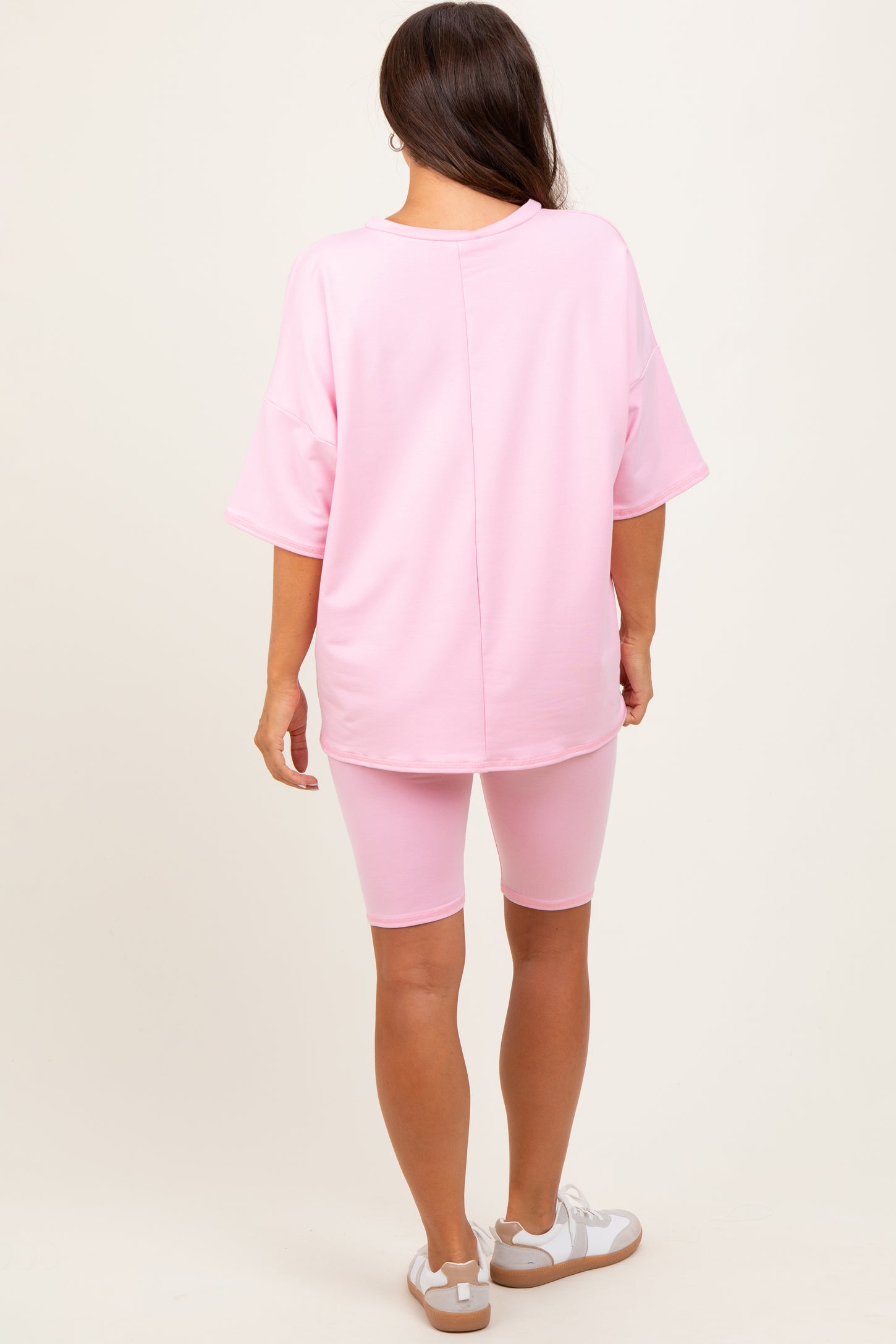 woman wearing a pink oversized maternity top and matching biker shorts, showing a relaxed fit from the back
