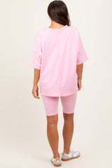 woman wearing a pink oversized maternity top and matching biker shorts, showing a relaxed fit from the back