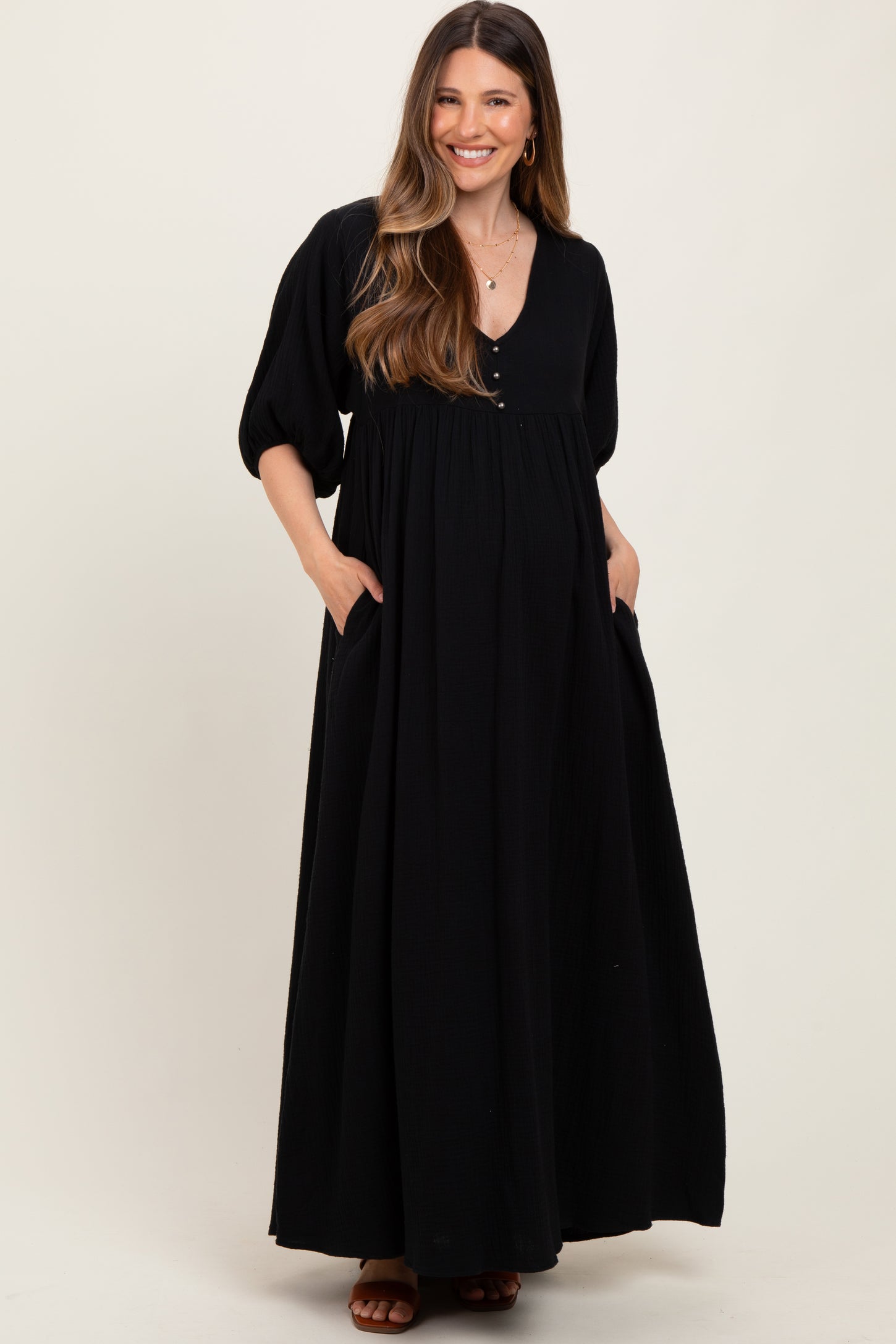 woman wearing a black maxi maternity dress with a v-neckline and puff sleeves, showcasing her baby bump