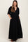 woman wearing a black maxi maternity dress with a v-neckline and puff sleeves, showcasing her baby bump