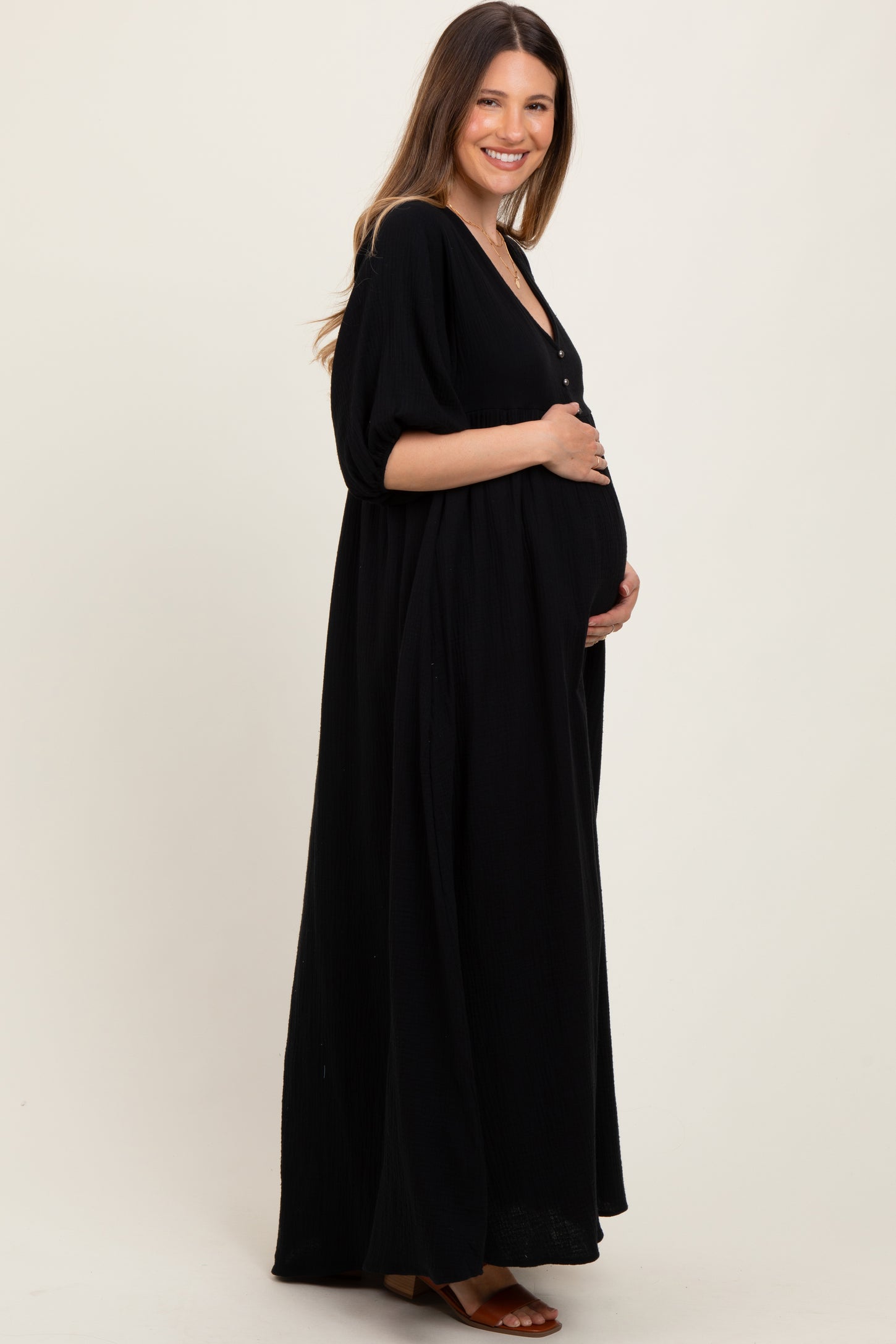 woman wearing a black maxi maternity dress with a button-down front and holding her baby bump